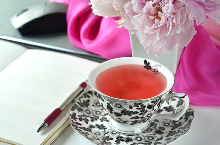 Elegant styled feminine desktop - relaxation, reading, creative writing, learning and journaling concept - with pink peonies, fruit tea and stylish stationeryの写真素材
