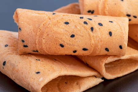 rolled wafer called "thong muan" made from flour, egg, sugar, sesame, coconut milk on black dishの写真素材