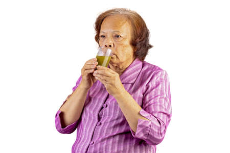Old aged asian woman drinking green tea by using two hands isolated on white backgroundの写真素材