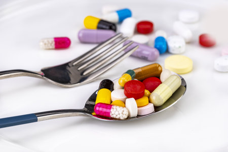 Several mixed medicine pills full on metal spoon on white plate with fork, healthy diet concept.の写真素材