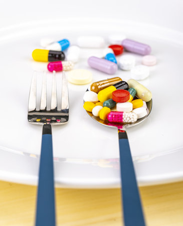 Several mixed medicine pills full on metal spoon on white plate with fork, healthy diet concept.の写真素材