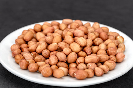 A lot of flesh raw peanuts on a white plate, ready to cook.
