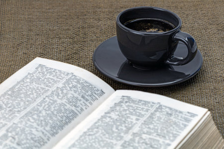 Black coffee in a black cup on a black saucer with a book and morning essentials on the table.の写真素材