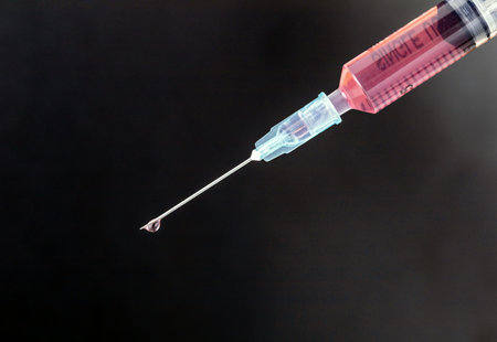 Syringe with red liquid on a black background representing medical injection and healthcare.の写真素材