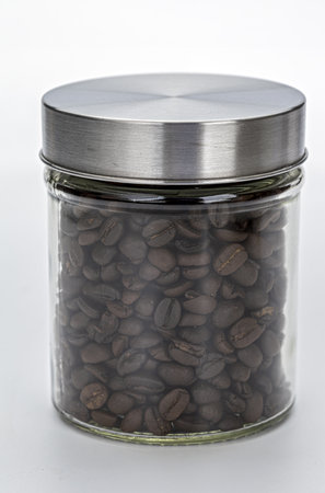 A glass jar filled with roasted coffee beans is sealed with metal lid, showcasing rich texture and dark color of beans. jar is placed against plain background, highlighting its contentsの写真素材