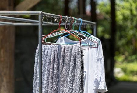 A clothes drying on hangers outside on metal rack, with towel and shirt in sunny garden setting....