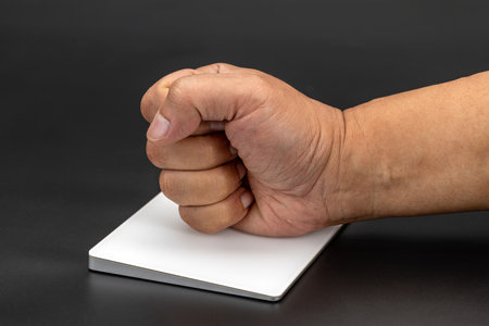 A clenched fist rests on white trackpad against dark background, conveying sense of determination or...