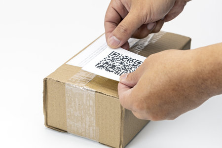 A hands placing dummy qr code label on cardboard shipping box, symbolizing modern logistics and efficient package tracking. scene highlights integration of technology in shipping processesの写真素材