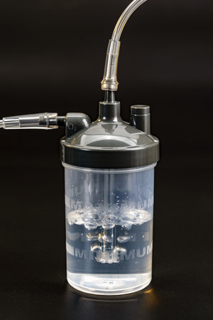 A clear oxygen humidifier bottle with black lid and attached tubing, used in medical settings to humidify oxygen for patients, is shown against dark background. bubbles are visible inside bottleの写真素材