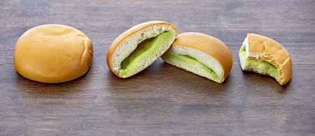 Three stages of pandanus custard bread on a wooden plate one whole, one cut in half, and one partially eaten, showing its soft texture and sweet filling.の写真素材