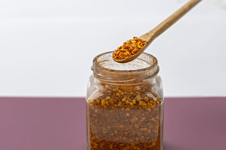 A wooden spoon with chili flakes above glass jar spicy seasoning dried red pepper kitchen ingredient...
