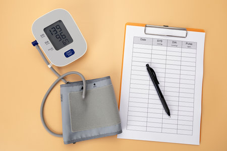A blood pressure monitor with log pad and pen on table, showing hypertension care through daily self tracking of health data.の写真素材