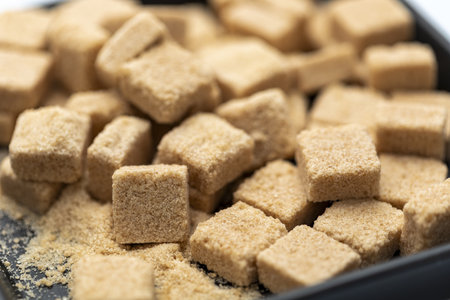 An organic brown sugar cubes in black bowl close up natural sweetener textured surface healthy ingredient rustic kitchen soft focus delicious and invitingの写真素材