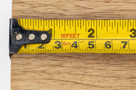 A yellow tape measure metal hook measurement scale metric imperial wood plank close up workshop...