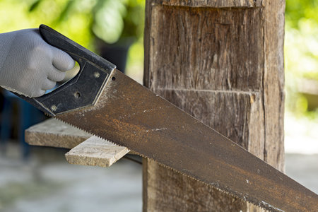 A hand saw is being used to cut wooden plank outdoors, showcasing close up of tool and wood. person...
