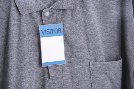 A visitor badge is attached to gray shirt, featuring collar and pocket. badge is prominently displayed, indicating temporary guest statusの写真素材