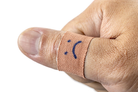 A thumb wrapped in bandage with sad face drawn on it, conveying sense of injury or discomfort. close...