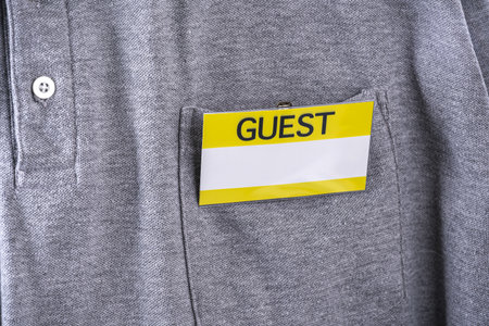 A guest badge with yellow border is clipped to pocket of gray shirt, indicating visitor status. badge stands out against fabric, suggesting formal or organized eventの写真素材