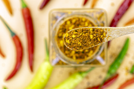 A close-up view of a wooden spoon holding spicy chili flakes with a jar of chili flakes in the...