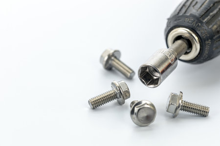 A close-up image of a socket wrench attached to a drill, surrounded by several shiny steel bolts...