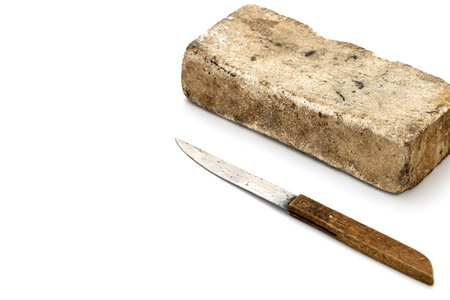 Still life featuring a big thick whetstone alongside a small, rustic knife with a wooden handle, positioned against a clean white backdrop. The image has a simple, utilitarian feel.の写真素材
