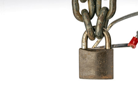 The photograph captures in detail a weathered locked padlock connected to an industrial chain. The...