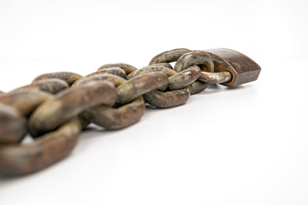 A heavy, rusted metal chain with an old padlock laid on a pristine white background. The image...