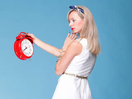 Portrait of pretty young woman in white dress against blue background timer red clockの写真素材