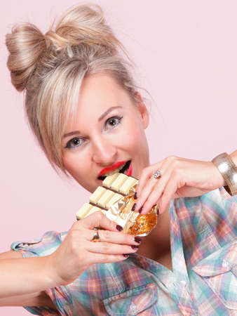 Cheerful pin up girl retro style portrait pinup Woman eating chocolate pink backgroundの写真素材
