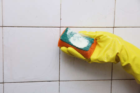 gloved hand cleaning dirty old tiles with sponge in a bathroomの写真素材