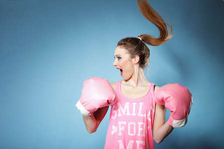Female boxer model wearing big fun pink gloves playing sports boxing hair motion, blue background