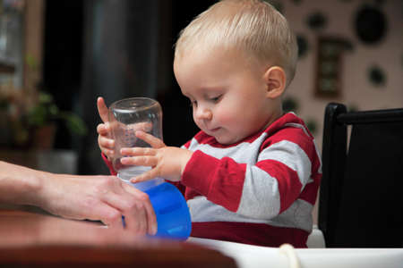baby boy playing with bottle and mug drinking indoor