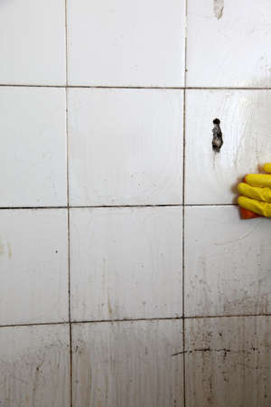 gloved hand cleaning dirty old tiles with sponge in a bathroomの写真素材