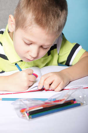 little boy drawing with color pencils on blue background
