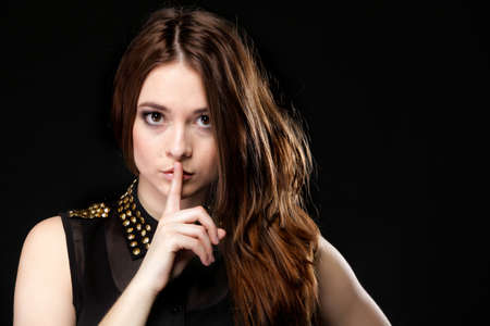 Secret woman. Female showing hand silence sign, saying hush be quiet on black backgroundの写真素材