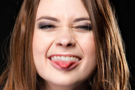 Grimacing young woman making silly face sticking out her tongue on black backgroundの写真素材