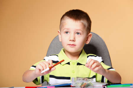 little boy drawing with color pencils on orange background