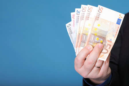 Euro banknotes in male hand on blue backgroundの写真素材
