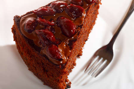 Piece of chocolate cake with icing and cherry on white background