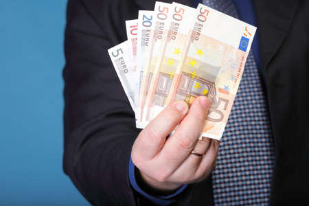 Euro banknotes in male hand on blue background