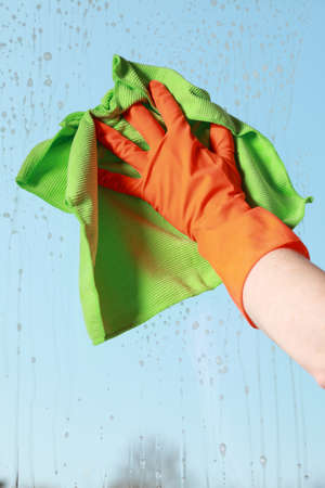hand in orange glove cleaning window with green ragの写真素材