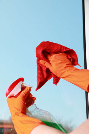 hand in orange glove cleaning window with red rag and spray detergent. Spring cleaning conceptの写真素材