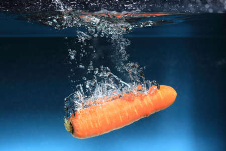 Carrot in the water splash over blue background. Healthy food and active life.の写真素材