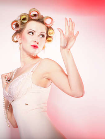 Sexy blonde woman preparing to party, girl in underwear with curlers in hair looking on nails pink...