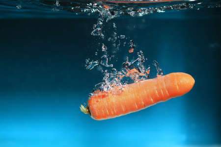 Carrot in the water splash over blue background. Healthy food and active life.の写真素材