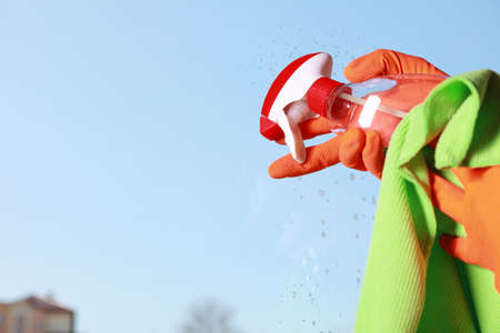 hand in orange glove cleaning window with rag and spray detergent. Spring cleaning concept