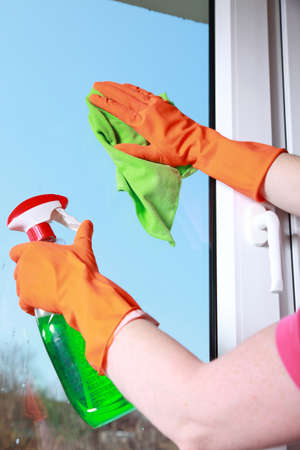 hand in orange glove cleaning window with green rag and spray detergent. Spring cleaning concept