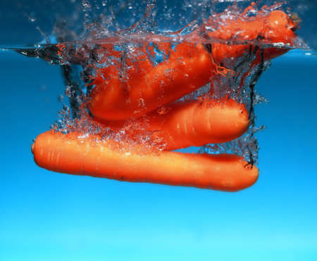 Carrot in the water splash over blue background. Healthy food and active life. Square formatの写真素材