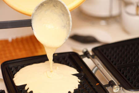 Waffle iron in the kitchen. Preparing homemade waffles, pouring a doughの写真素材