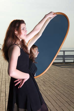 thoughtful young woman looks at the reflection in the mirror - solitude lonely conceptの写真素材